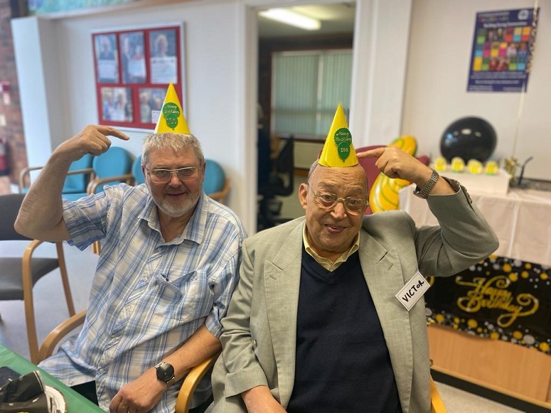 two-community-members-point-at-their-100-themed-birthday-hats