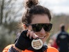 a-participant-smiles-holding-up-her-muddy-mayhem-finishers-medal