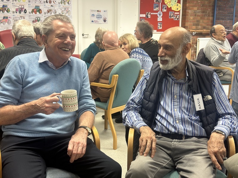 two-men-sitting-in-chairs-laughing-and-drinking-tea