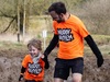 a-father-and-child-hold-hands-running-through-the-mud-at-muddy-mayhem