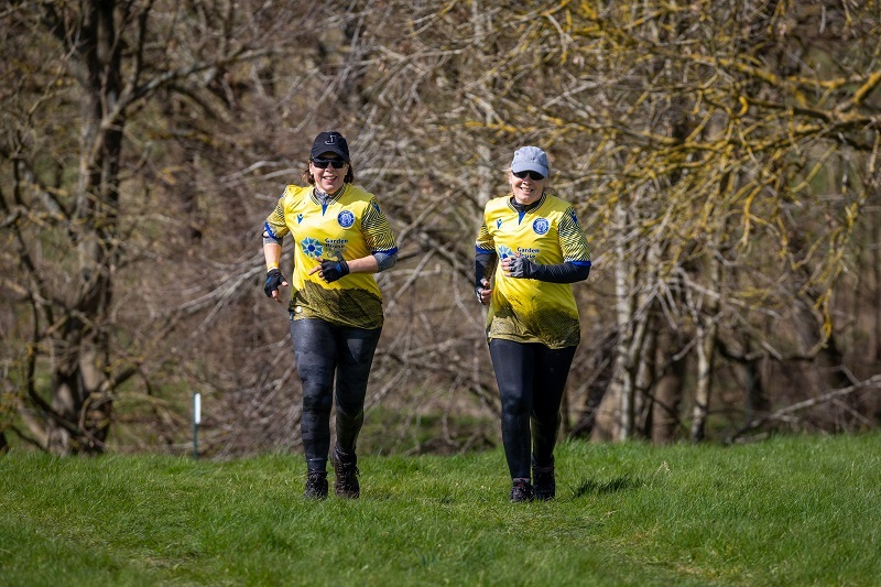 two-people-running-at-muddy-mayhem-wearing-stevenage-fc-third-shirt