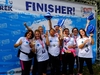 a-team-cheer-and-raise-their-hats-in-front-of-a-thames-bridges-trek-finisher-banner