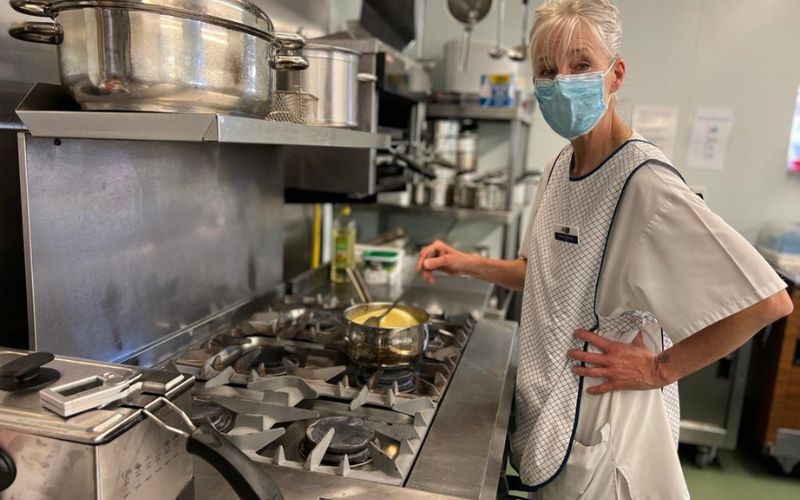 hospice-cook-wearing-apron-stirs-pot-on-oven