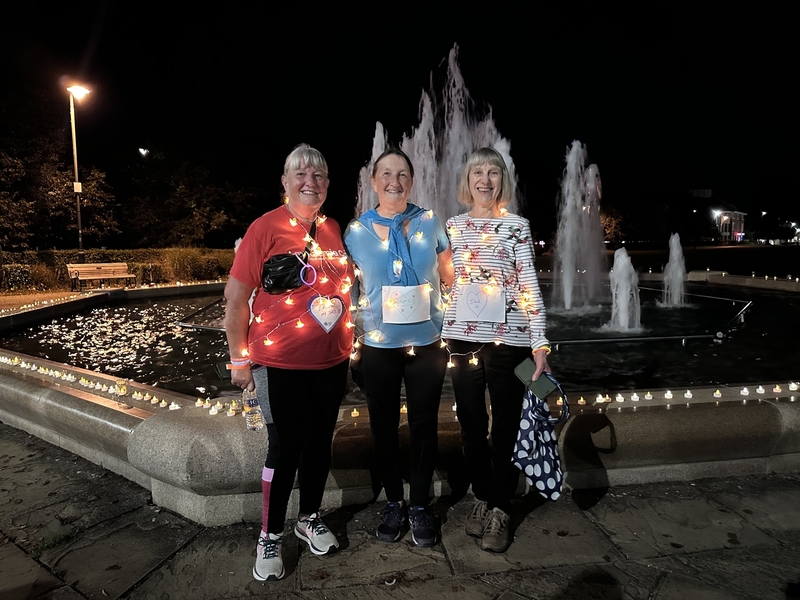 three-ladies-wrapped-in-fairy-lights-stand-in-front-of-fountain